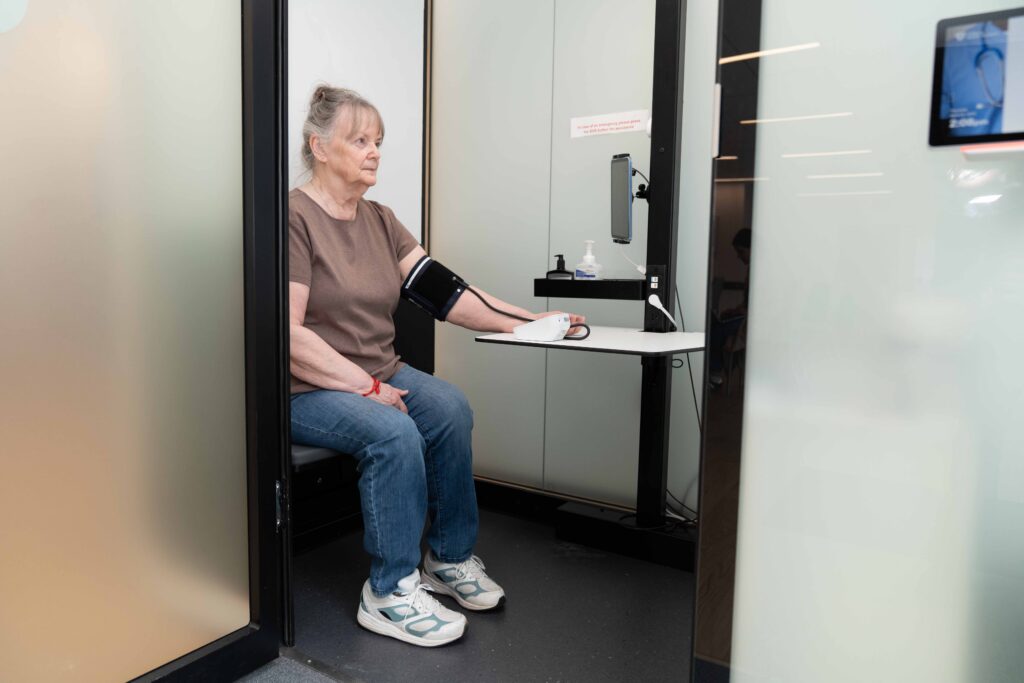 Elderly woman using remote health monitoring device in a clinical setting.
